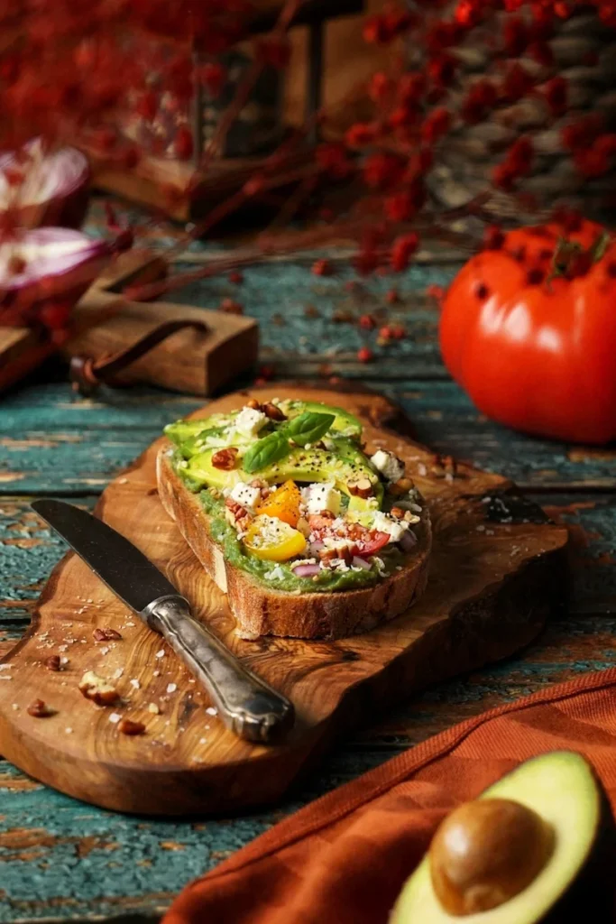 Frisches Avocado-Brot mit Feta, bunten Tomaten und Nüssen auf rustikalem Holzbrett in gemütlicher Atmosphäre, fotografiert von Studio Visionelle.