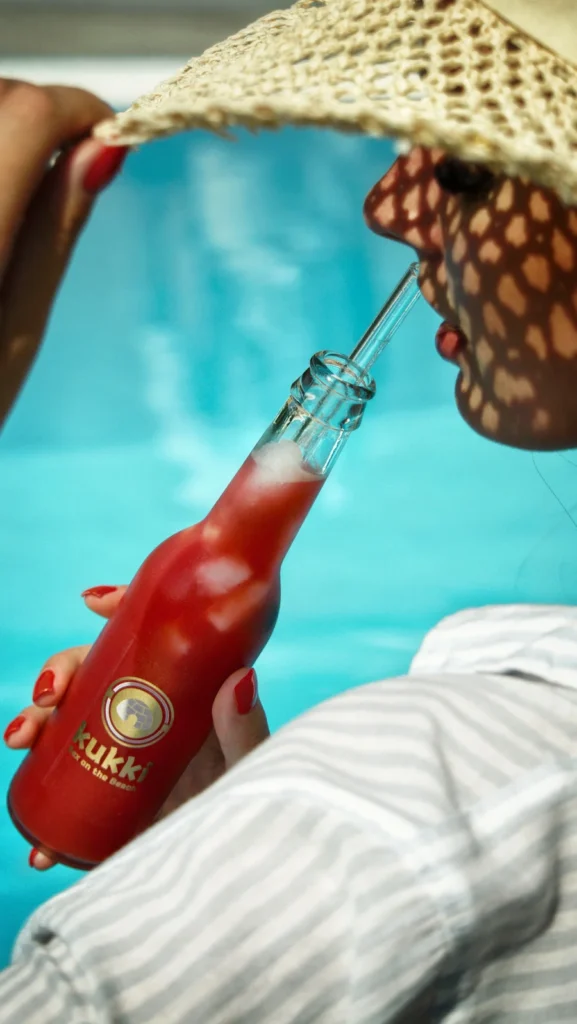 Kukki Cocktail am Pool mit Model mit Sonnenhut von hinten in sommerlicher Atmosphäre, fotografiert von Studio Visionelle.