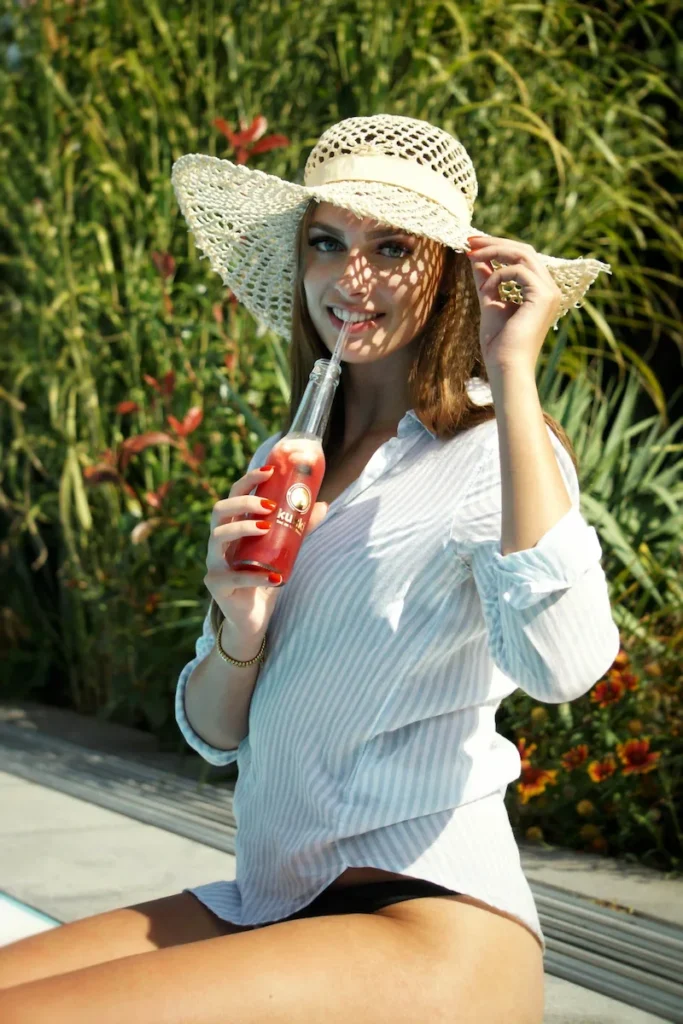 Studio Visionelle: Model mit Hut genießt einen Cocktail am Pool, während die Beine entspannt im Wasser hängen