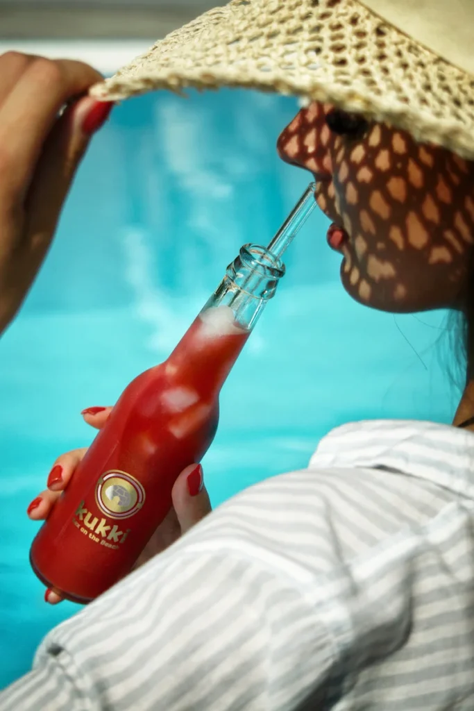Kukki Cocktail am Pool mit Model mit Sonnenhut von hinten in sommerlicher Atmosphäre, fotografiert von Studio Visionelle.