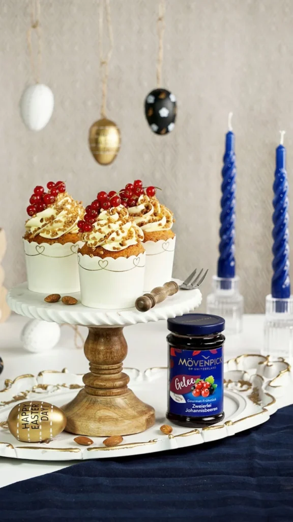 Cupcakes mit Sahne, Krokant und roten Johannisbeeren auf Tortenständer, daneben Mövenpick Gelee, stilvoll fotografiert von Studio Visionelle.
